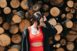 woman in red athletic wear stands in front of a stack of wood 身穿红色运动服的女人站在一堆木头前。